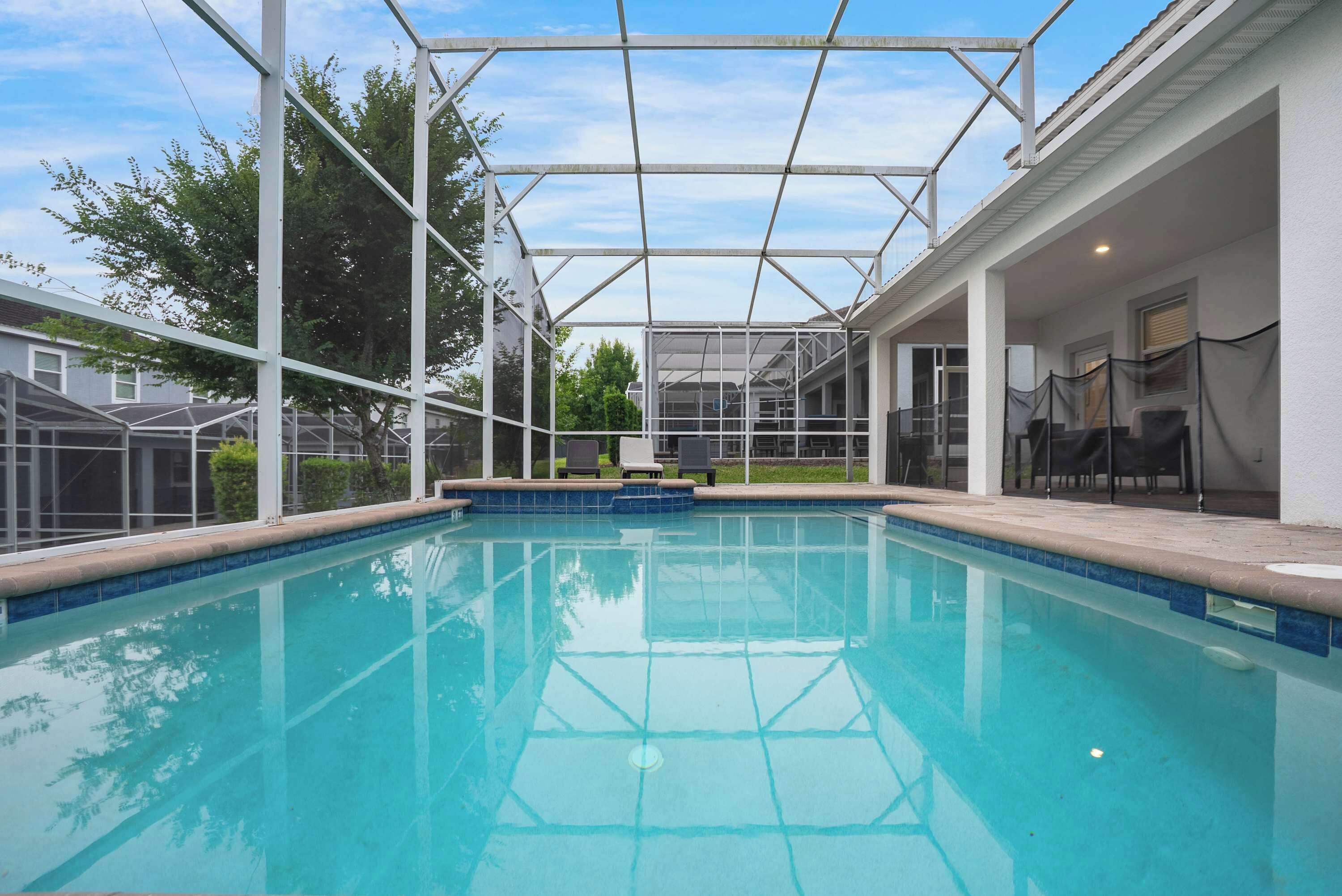 A swimming pool with a covered area, surrounded by a white building with a patio and outdoor seating.