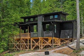 Une cabane à deux étages dotée d’une terrasse en bois, entourée d’une forêt dense.