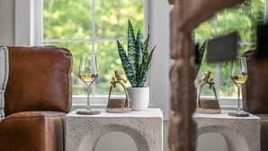 Una stanza con una finestra, una pianta in vaso, due sedie e due bicchieri di vino su un tavolo.