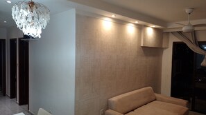 Un interior moderno con un papel tapiz estampado, una araña de cristal, luces empotradas en el techo, un sofá y una ventana con cortinas.