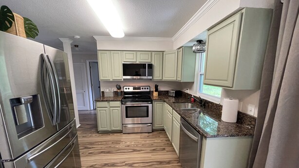 Una cocina con gabinetes verde claro, electrodomésticos de acero inoxidable y piso de madera.