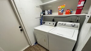 Una sala de lavandería con lavadora, secadora y repisas con artículos de limpieza.
