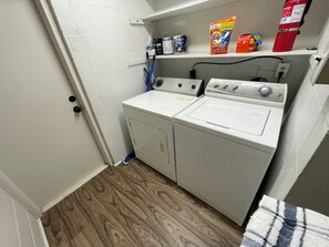 A laundry room with a washing machine, dryer, and shelves with cleaning supplies. - 8 minutes to WEC , Charming 3 bedroom home, on half acre , Fenced  on paved road (Ocala)