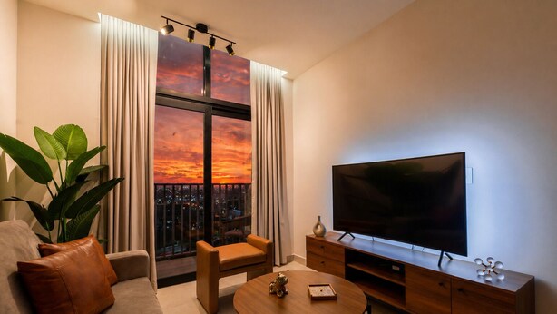Una sala moderna con un televisor grande, un sofá, una mesita de centro, una planta y vistas a un atardecer a través de una ventana.