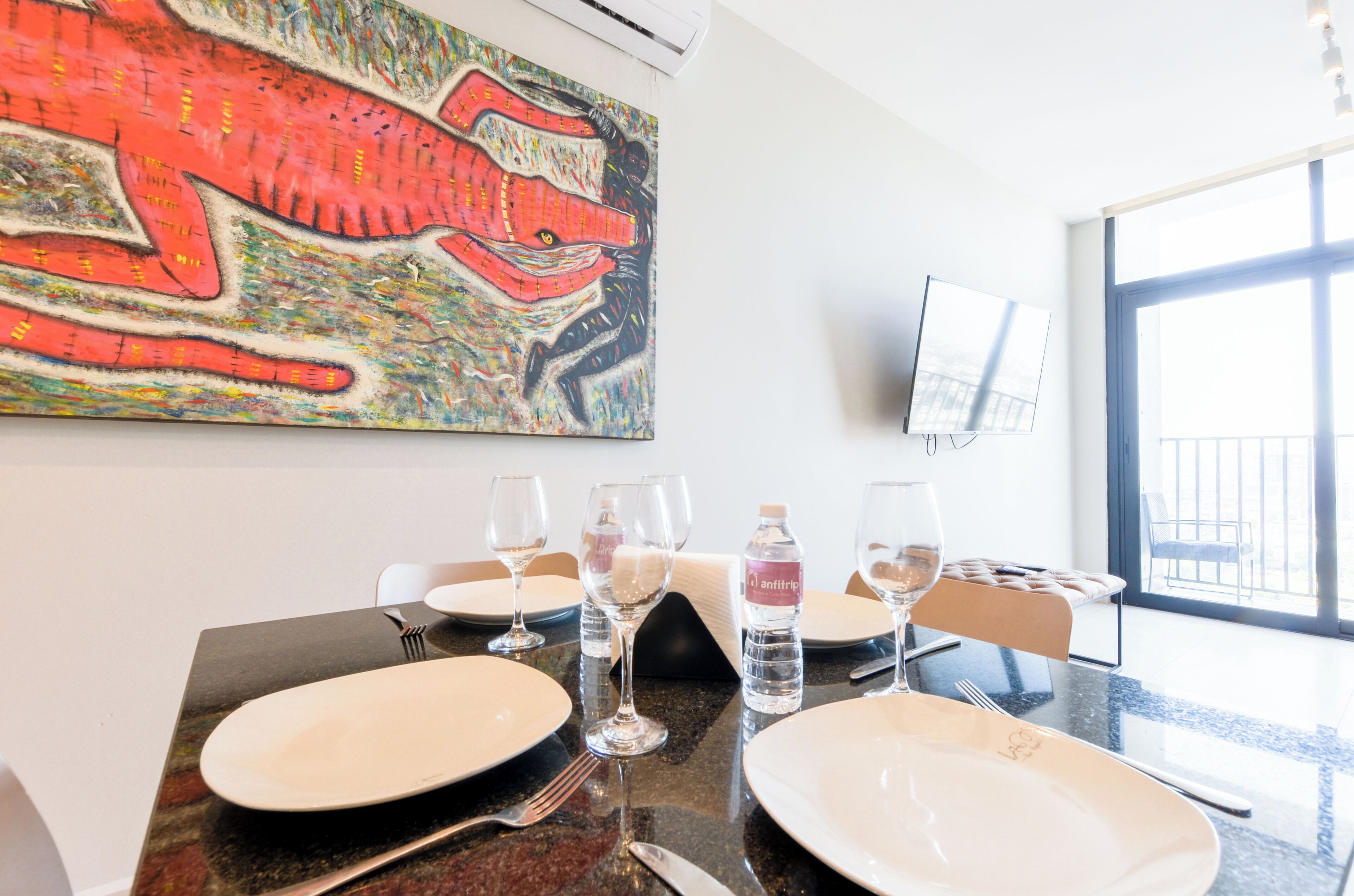 A dining table set with plates, glasses, and cutlery, a water bottle, and a painting on the wall.