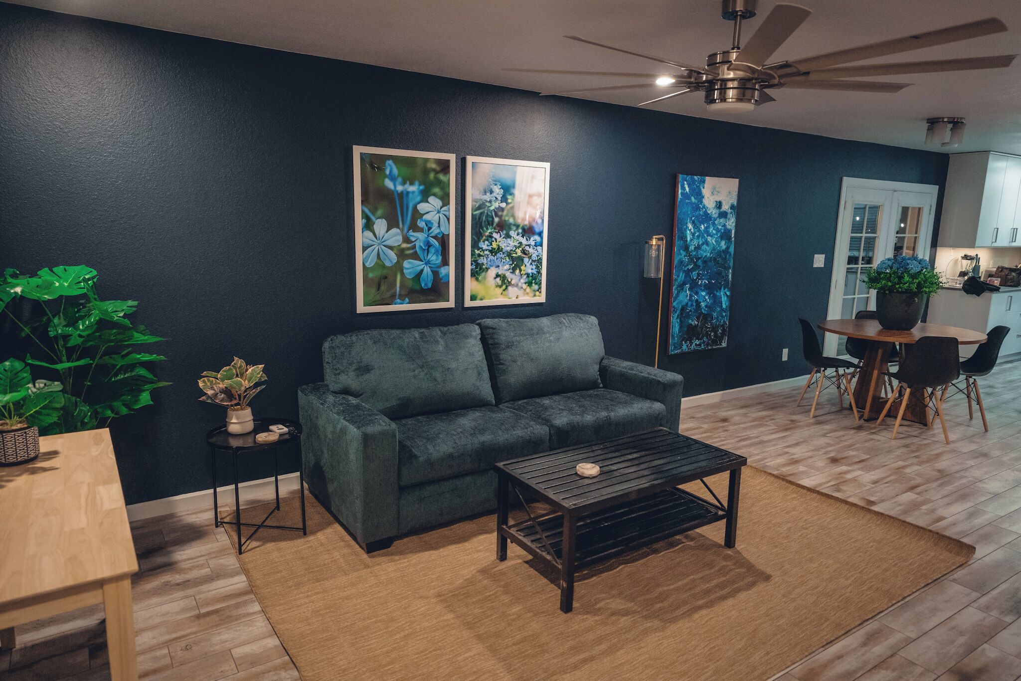 Una sala de estar con pared azul oscuro, sofá gris, mesa de centro de madera y ventilador de techo.