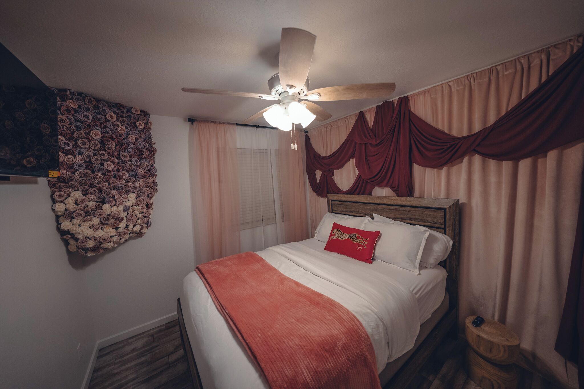 Una camera da letto con un letto, una ventola a soffitto, un arazzo appeso al muro e tende.