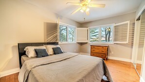Une chambre à coucher avec un lit, un ventilateur de plafond, une commode et des fenêtres équipées de stores.