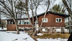 Une cabane en rondins, avec des fondations en pierre, de grandes fenêtres et un paysage enneigé.