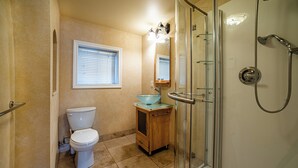 Une salle de bain comprenant des toilettes, un lavabo en verre, un miroir et une douche fermée par des parois de verre.