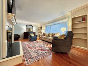 A living room with a sofa, armchairs, a rug, a fireplace, and a bookshelf.