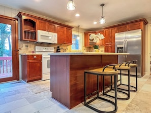 A kitchen with wooden cabinets, a stainless steel refrigerator, a built-in oven, and a bar area with stools.
