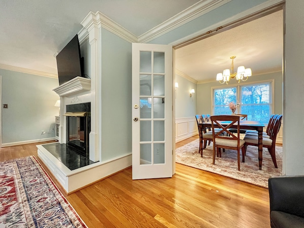 A dining area with a wooden table and chairs, a fireplace, and a view through an open door.