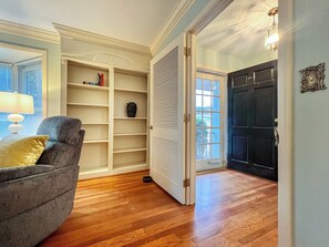 A room with a wooden floor, a chair, a bookshelf, a door, and a window.
