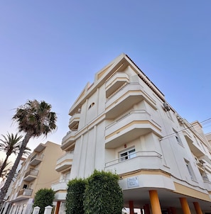 A multi-story building with balconies, a sign reading 'Avenida de la Marina,' and palm trees in the foreground.