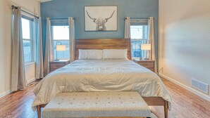 Een slaapkamer met een groot bed, een hoofdeinde, nachtkastjes en een raam met gordijnen.