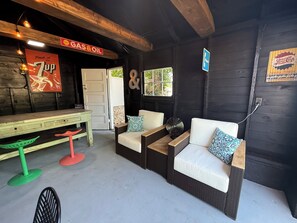 Un intérieur rustique avec un banc en bois, deux canapés blancs avec des coussins, un tabouret vert et rouge, et un ventilateur.