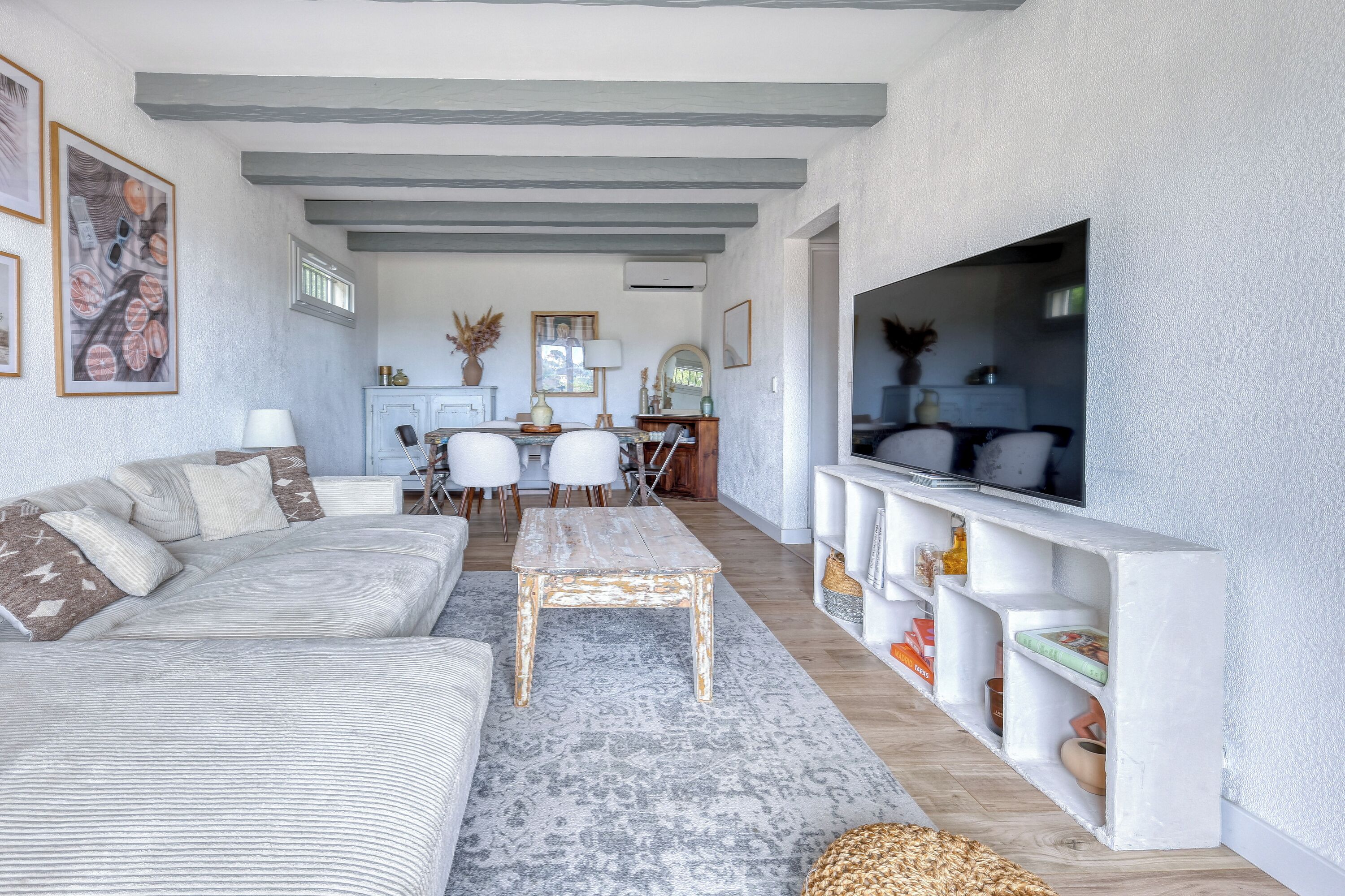 Ein Wohnzimmer mit einer Couch, einem Couchtisch, einem Fernseher auf einem weißen Regal und einem Essbereich mit Stühlen und einem Tisch.
