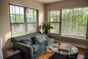 A living room with a sofa, a glass coffee table, and a potted plant. - 2-bedroom apartment in cool Detroit with refreshing AC (Detroit)
