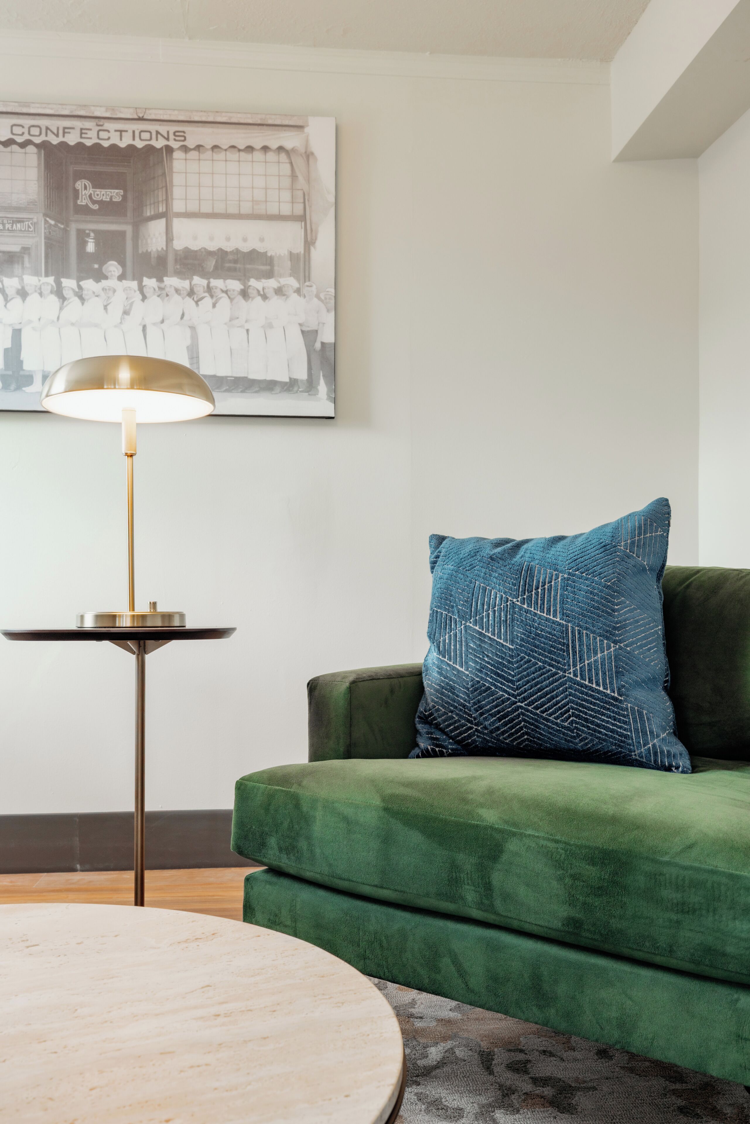 Un canapé vert agrémenté d’un coussin à motifs, une table basse ronde en bois et un lampadaire avec un pied doré.