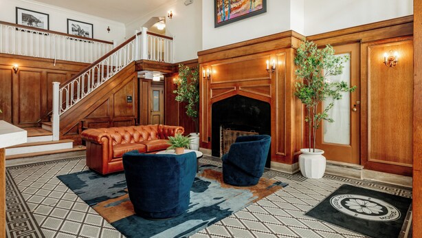 A spacious lobby with a grand staircase, a fireplace, and a large painting on the wall. - Eugene Hotel (Monroe)