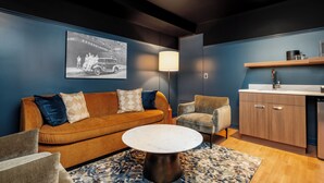 A modern living room with a sofa, armchairs, a coffee table, and a kitchen area with cabinets and a sink. - Eugene Hotel (Monroe)