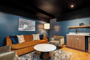 Una sala de estar moderna con un sofá, sillones, una mesa de centro y una zona de cocina con armarios y un lavamanos.