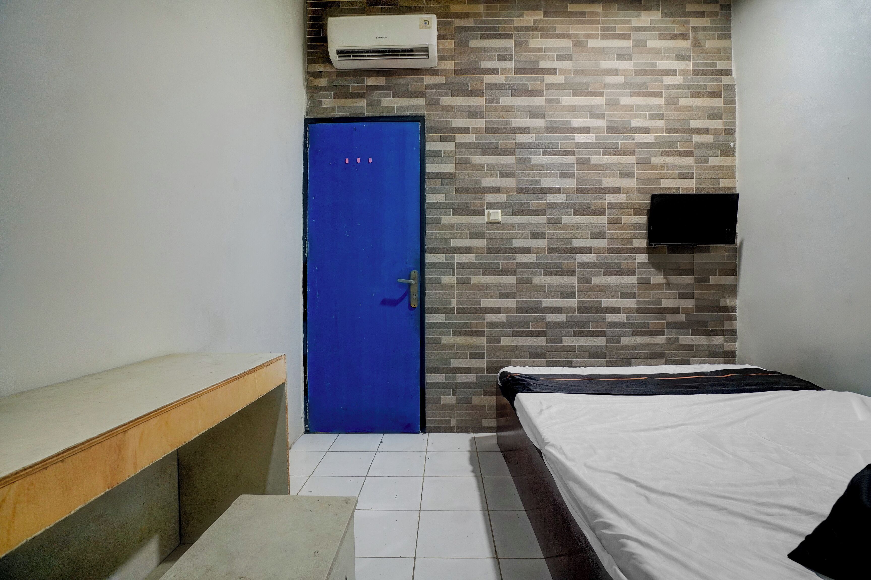 A room with a blue door, a bed with white bedding, a bench, and a tiled floor.
