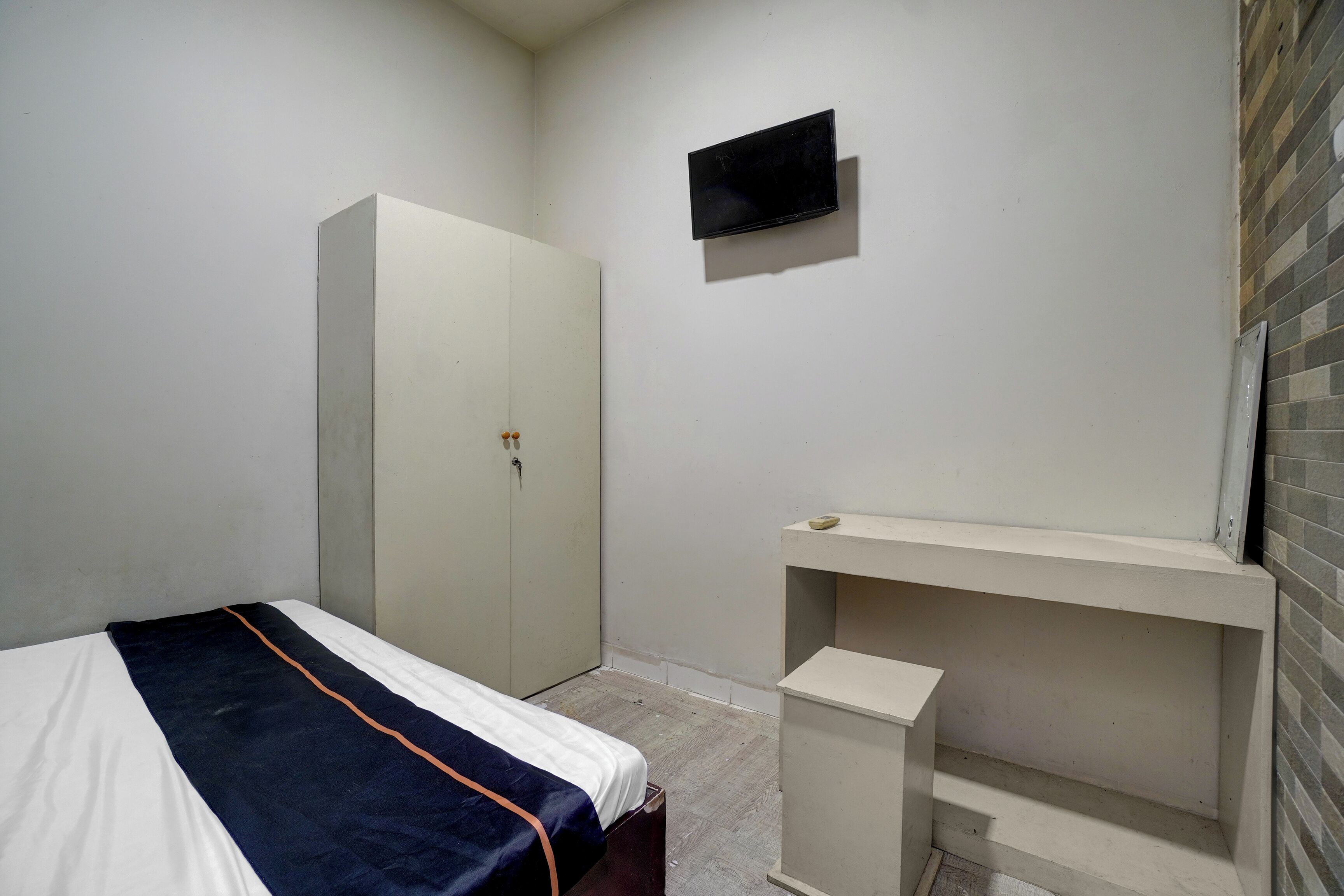 A bedroom with a bed, a wardrobe, a television, and a small desk.