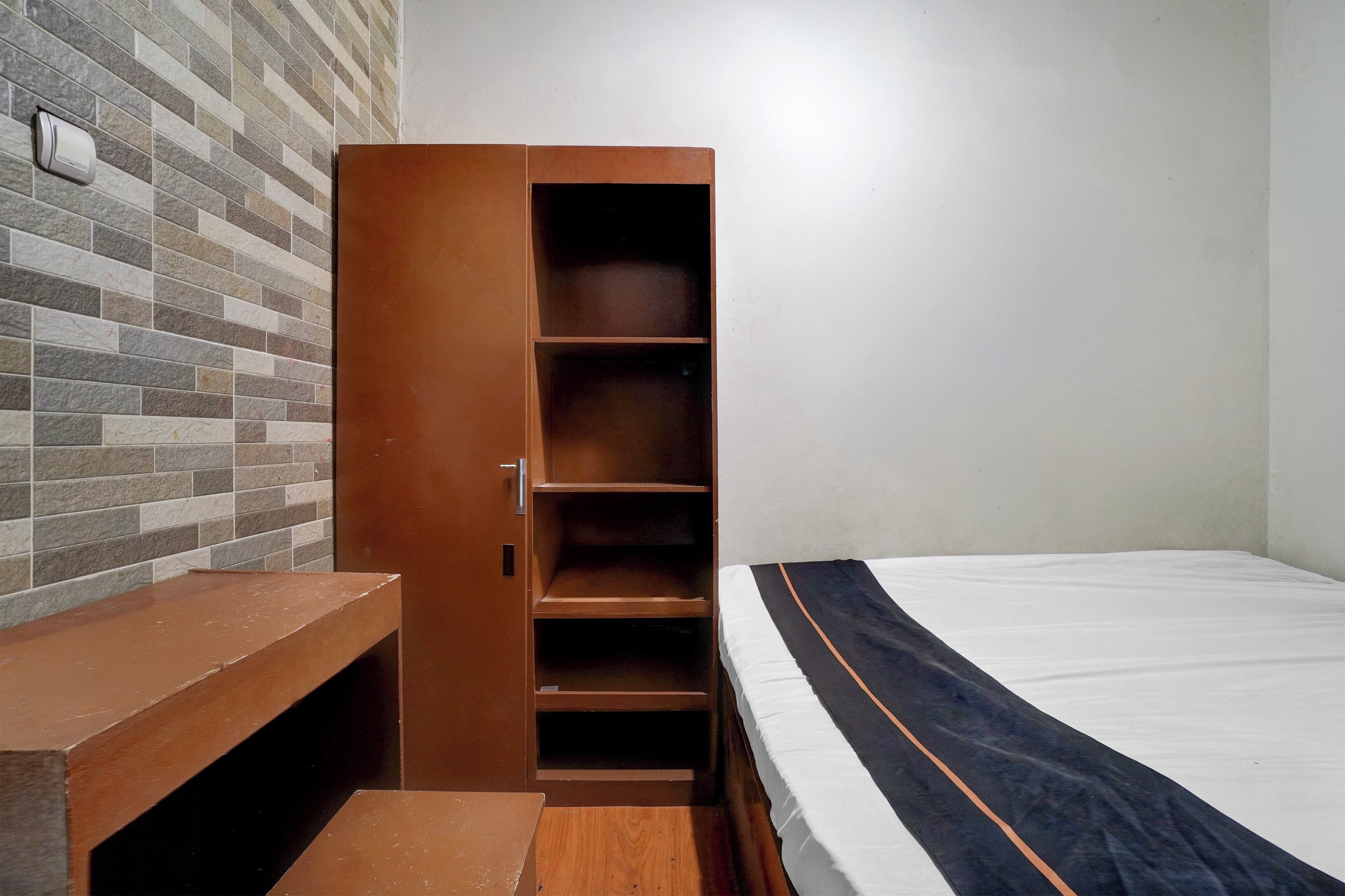 A room with a bed, a wooden wardrobe, a bench, and a tiled wall.