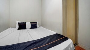 A single bed with white bedding and a black and orange striped blanket, a white pillow, and a black pillow. - Hotel O near RS Husada formerly Pondokan (Jakarta)