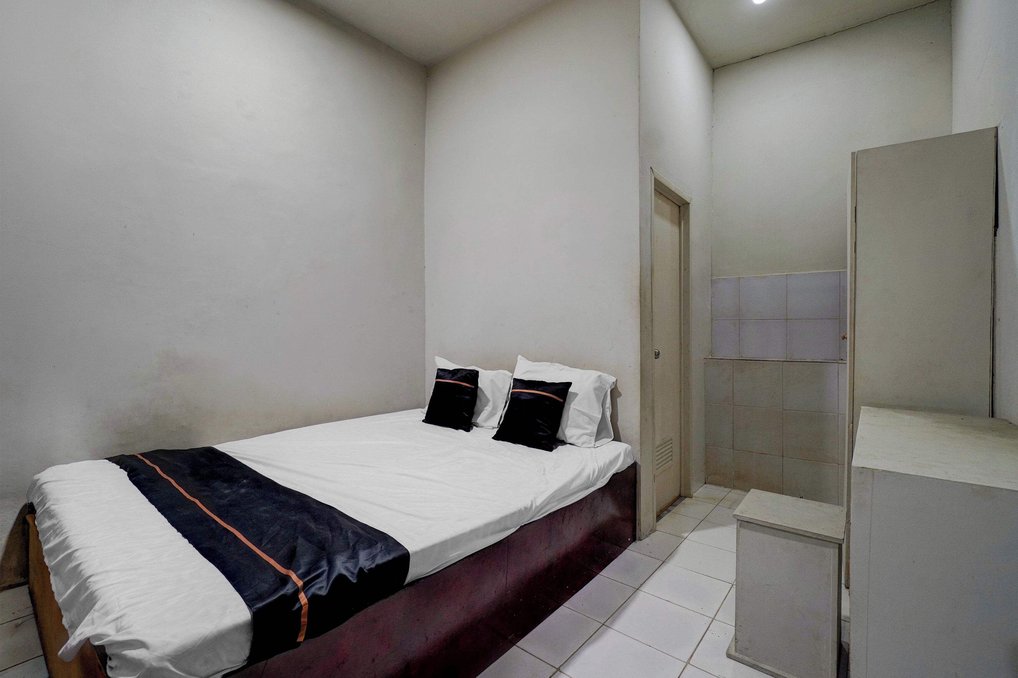 A bedroom with a bed, a bench, a door, and a mirror.