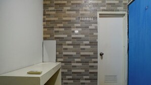 A bathroom with a tiled wall, a white bench, a door, and a blue wall. - Hotel O near RS Husada formerly Pondokan (Jakarta)