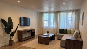 A living room with a flat-screen TV, a wooden coffee table, a sofa, and a potted plant.