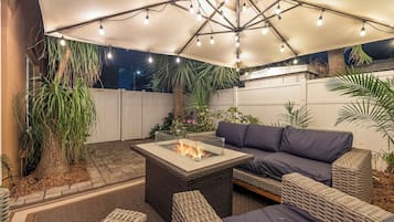 A covered outdoor seating area with a fire feature, wicker furniture, and potted plants.