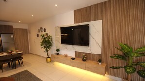Eine moderne Küche mit Einbaukühlschrank, eine Essecke mit Tisch und Stühlen sowie ein Wohnbereich mit an der Wand befestigtem Fernseher.