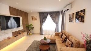Ein modernes Wohnzimmer mit einer Couch, einem Couchtisch, einem Fernseher und einem großen Fenster mit Vorhängen.