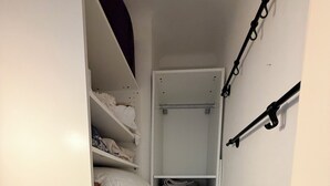 Um closet pequeno com prateleiras para roupas dobradas, uma barra para pendurar e um cesto organizador.