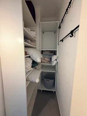 Ein schmaler begehbarer Kleiderschrank mit Regalen für gefaltete Kleidung, einer Kleiderstange und einer Aufbewahrungsbox.