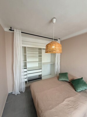 Ein Schlafzimmer mit einem Bett, einer hängenden Korblampe, einem Kleiderschrank mit Regalen und transparenten Vorhängen.