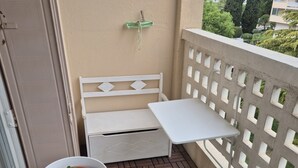 Uma varanda com um banco branco, uma mesa pequena com planta em vaso e vista para edifícios e árvores.