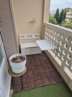 Ein Balkon mit einer weißen Bank, einem kleinen Tisch mit einem Topfpflanzen und Blick auf Gebäude und Bäume.
