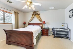 A bedroom with a wooden bed, a ceiling fan, a nightstand with a lamp, and a crib.