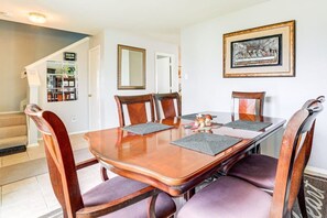A dining room with a wooden table, four chairs, a framed picture on the wall, and a staircase in the background.