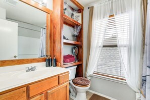 A bathroom with a wooden vanity, a large mirror, a toilet with a wooden seat, and a window with blinds.