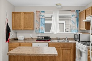 A compact kitchen with wooden cabinets, a built-in dishwasher, a microwave, and a stove. - Katy Family Home with Patio Pergola and Grill (Katy)