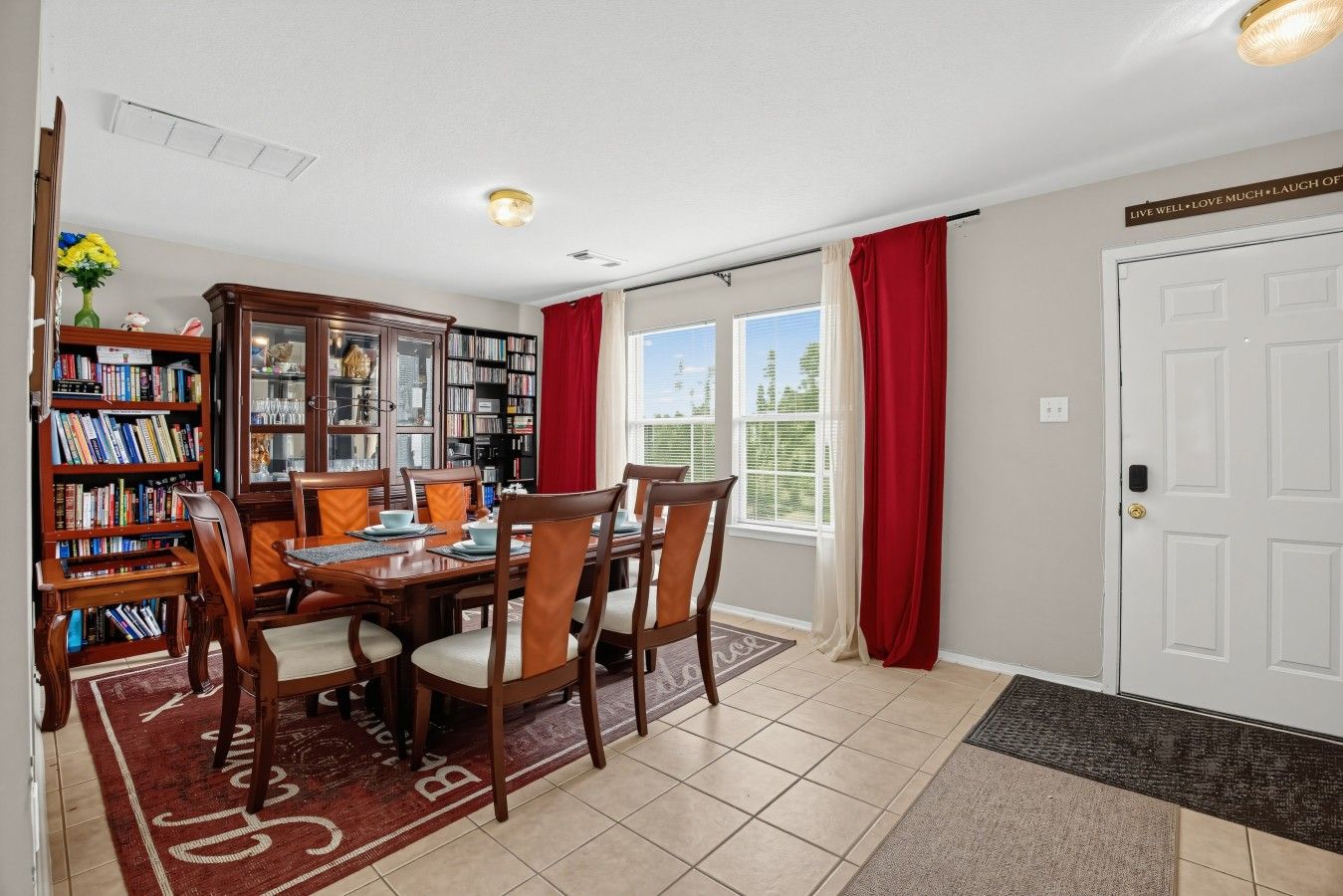 A dining area with a wooden table and chairs, a bookshelf, and a view through a sliding glass door.
