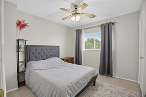 A bedroom with a bed, a nightstand, a ceiling fan, a window with curtains, and a wall-mounted shelf with a globe. - Katy Family Home with Patio Pergola and Grill (Katy)