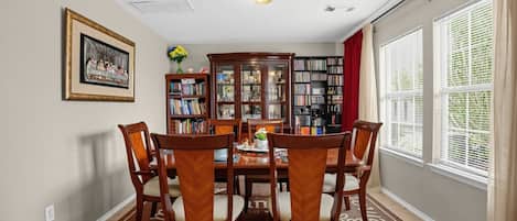 A dining room with a wooden table and chairs, surrounded by bookshelves and a framed picture on the wall.