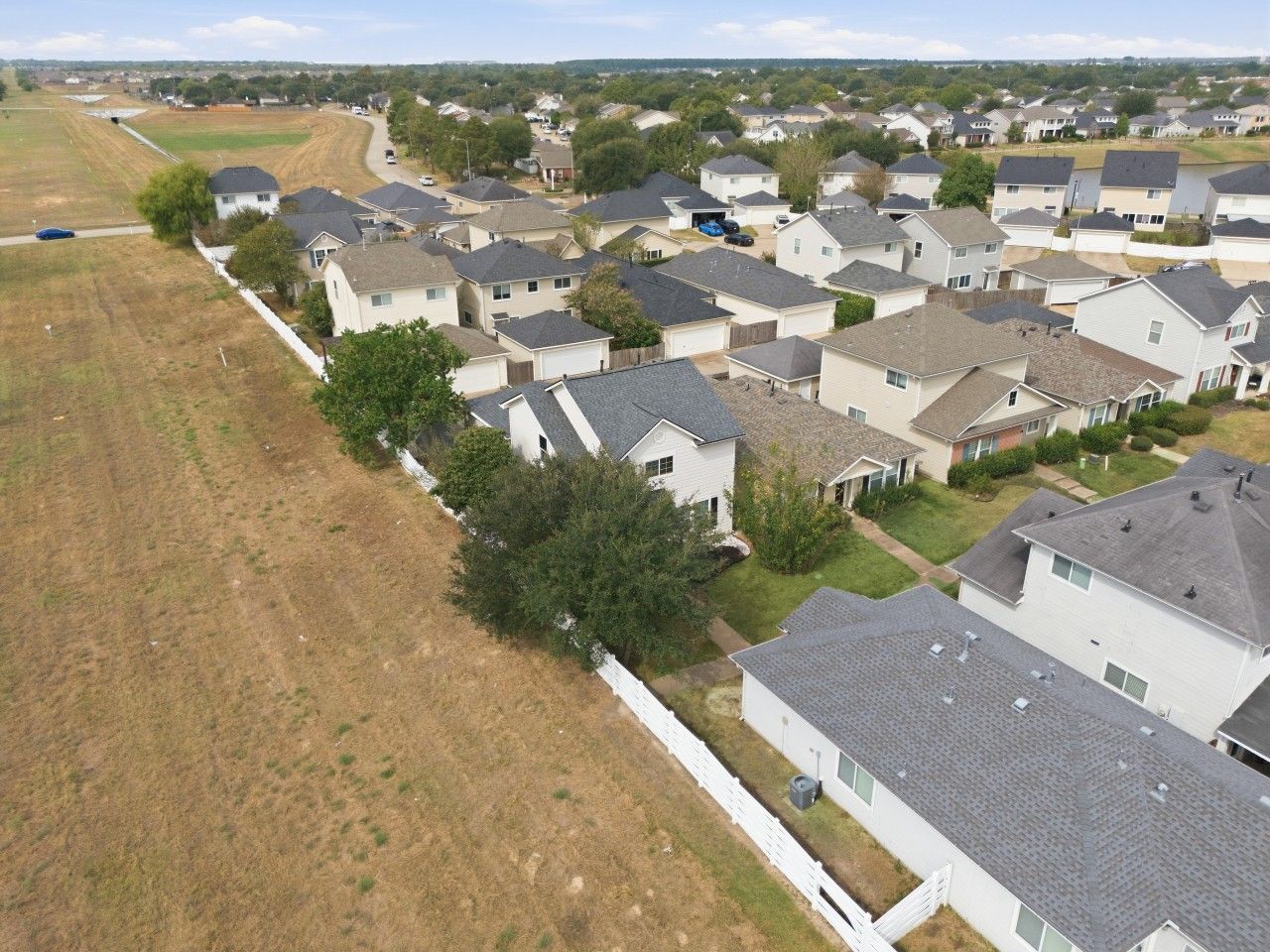 Un quartier résidentiel avec des maisons, une clôture blanche et un champ d’herbe.